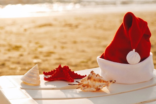 Santa Claus Hat on sunbed near tropical calm beach with turquoise caribbean sea water and white sand. Christmas vacation celebration . Starfish in red santa hat at the seaside. Christmas in summer